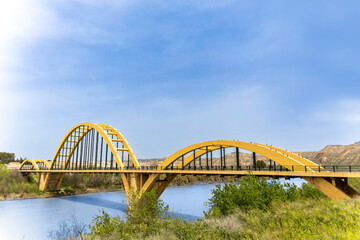 A yellow bridge spans a river, with a clear blue sky above