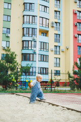 Obraz premium A toddler boy in denim overalls runs and plays on the playground. Active time of the child outside. A child runs on the street in the summer.