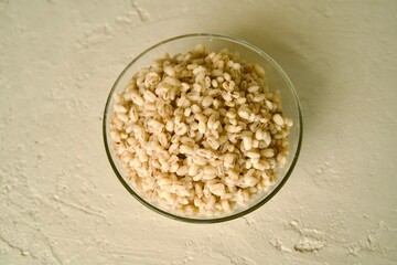A glass bowl filled with cooked pearl barley on a light surface.