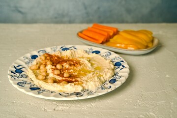 Hummus on a ceramic plate sprinkled with smoked paprika and drizzled with olive oil on a light surface.