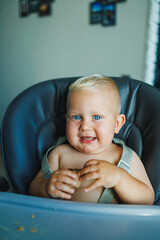 A little baby boy is sitting in a high chair. An emotional child sits in a chair and eats. Feeding a child.