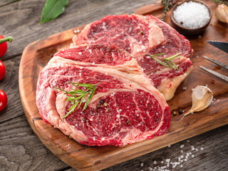 Raw beef steaks with herbs and spices ready for cooking are on wooden board.