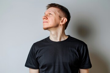 A man wearing a black T shirt standing in front of a white background and taking a deep breath