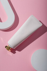 White unbranded cosmetics tube mockup, concrete decor on pink background. Beauty product template, advertising banner. Copy space. Flay lay, top view