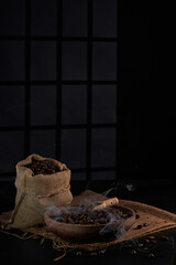 Photo of a coffee grinder with a bag of coffee beans, a coffee spoon, a cup of coffee and coffee beans on a dark window background