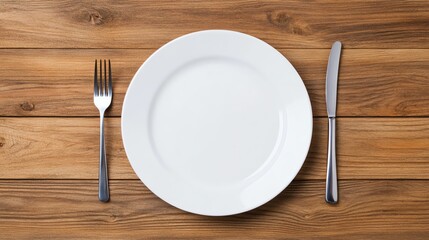 Empty white plate with fork and knife on wooden table, top view.