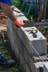 A bricklayer works on blocks to build a wall on a construction site with concrete, a trowel, a level and a grinder