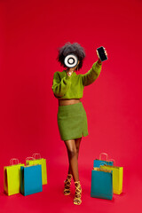 Woman in green sweater holds megaphone and smartphone, standing confidently with shopping bags on red background. Concept of marketing, retail, communication, online shopping, betting,