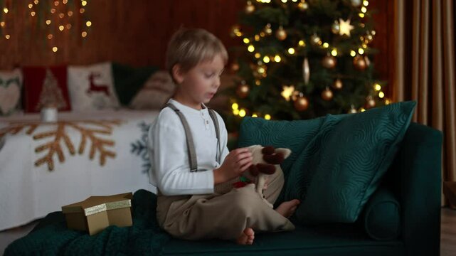 Sweet blond child, cute boy, playing with christmas toys on Christmas, beautifully decorated home for Christmas, cosy place