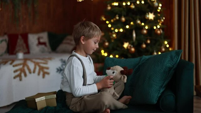 Sweet blond child, cute boy, playing with christmas toys on Christmas, beautifully decorated home for Christmas, cosy place