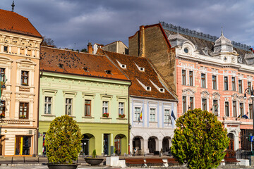 Fototapeta premium Brașov's autumn square charm. Colorful buildings line the square in Brașov, Romania, showcasing historical architecture against a cloudy autumn sky.