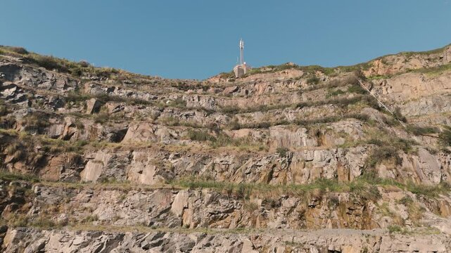 Panning and rising footage of terraced granite quarry and industrial buildings Les Vardes Quarry Guernsey on bright day