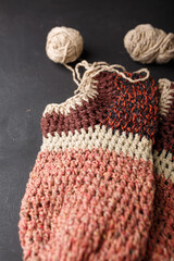 Two crochet socks on black background, copy space. Brown and beige crocheting yarn balls, footwear making process, close up