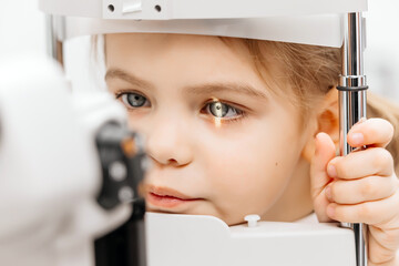 Examination of a little girl's eyes in an ophthalmology clinic. A laser beam shines into the...