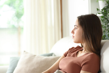 Serious woman looking through a window sitting at home