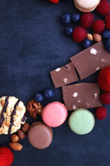 Macarons, chocolate, cookies, berries and various nuts on dark blue background. Top view.
