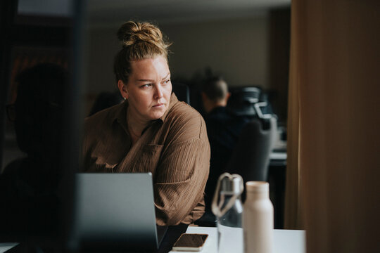 Thoughtful businesswoman sitting with laptop near desk at office
