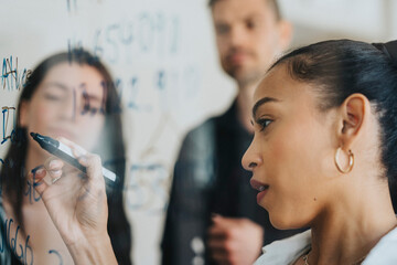 Female business professional writing statistics on glass board at office