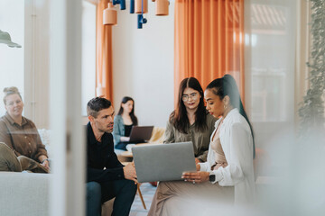 Female business professional discussing with colleagues while using laptop at workplace