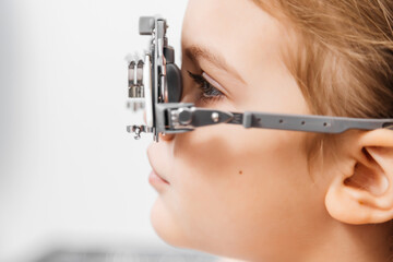 A pediatric optometrist examines the eyes of a little girl using modern equipment. The happy girl...