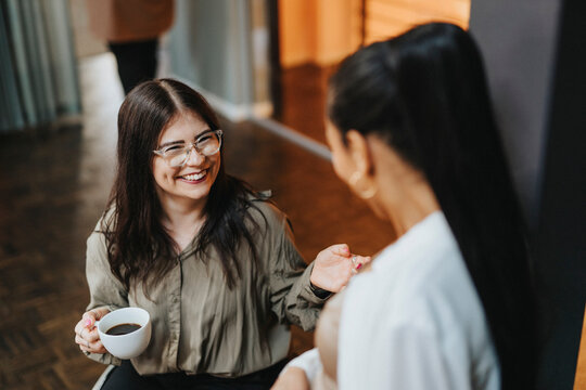 High angle view of happy female entrepreneur holding coffee cup and discussing with colleague in office