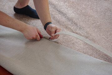Closeup of male craftsman's hands laying carpet on floor. Professional fitting carpet in an...