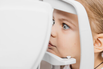 A pediatric optometrist examines the eyes of a little girl using modern equipment. The happy girl...