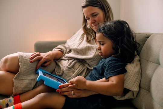 Mother and son spending leisure time watching digital tablet while sitting on sofa at home