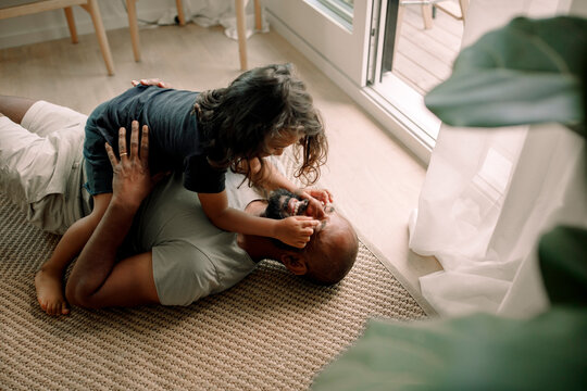 High angle view of boy playing with father's eyes lying down on carpet at home