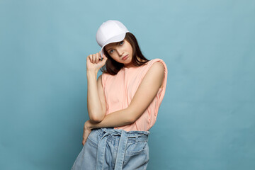 Young woman, teenager, in white cap and pink T-shirt on blue background. Model posing, close-up,...
