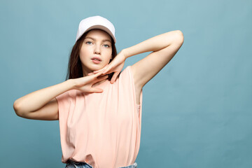 Fototapeta premium Young woman, teenager, in white cap and pink T-shirt on blue background. Model posing, close-up, emotion. Copy space