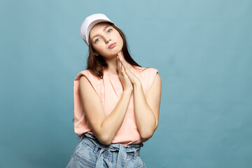 Young woman, teenager, in white cap and pink T-shirt on blue background. Model posing, close-up, emotion. Copy space