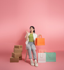 Portrait of Asian woman posing on pink background, next to shopping bags.