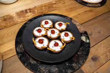 A plate of delicious buns in the shape of reindeers with a cherry as a nose on a black plate on a wooden kitchen table