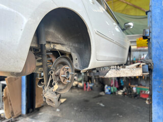 A car rear wheel assembly is elevated, revealing the brake drum and suspension components, indicating maintenance work in progress. The environment is a busy garage.