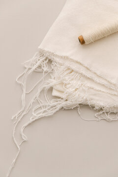 Messily folded white ragged fabric and ecru tread on bobbin on a light table top.