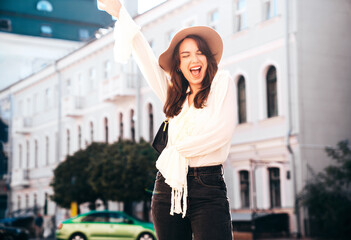 Fototapeta premium Portrait of young beautiful smiling hipster woman in trendy summer white blouse and jeans. Carefree woman posing in the street in sunny day. Positive model outdoors. Cheerful and happy