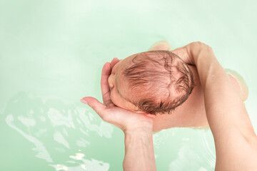 Top view of newborn baby held in water during bath time