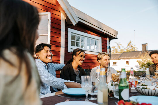 Happy male and female friends sitting together at dining table in back yard for dinner party