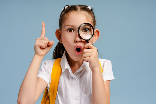 Surprised schoolgirl looking through magnifying glass having an idea