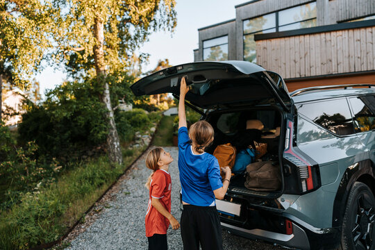 Boy closing car trunk while standing with brother on driveway by house