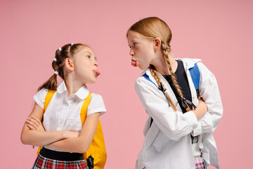 Two schoolgirls sticking out tongues at each other on pink background