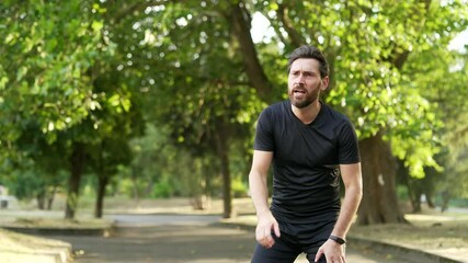 Adult runner has shortness of breath during a run in city park. Athlete feels tired. Sportsman rests his hands on his knees, taking a rest break, he's breathing heavily after intense physical activity - Powered by Adobe