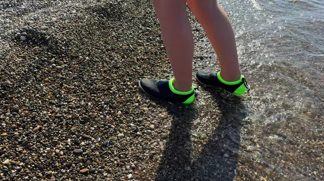 Close-up of slim legs of female walking down pebbles over blue sparkling background