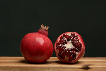 Photograph of the red pomegranates on a wooden board, the whole and open with juicy edible seeds. Sweet, tart fruit, high in antioxidants such as polyphenols. Healthy eating. Five a day. 