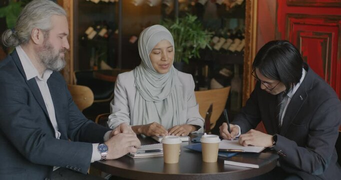 Two businessmen talking and signing contract during business meeting with female translator in cafe. Agreement and interpreter service concept.