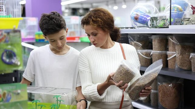 Mom and son are preparing to provide comfortable stay for new pet, choose high-quality and healthy food for turtles in pet store, read composition of product on label
