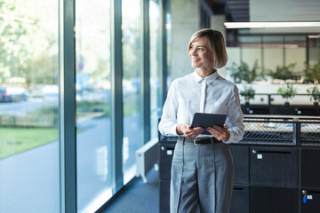 Smiling busy young businesswoman manager using tablet computer, executive looking out the window...