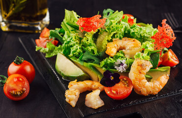 Fresh salad with shrimps, avocado and cherry tomatoes on black wooden table