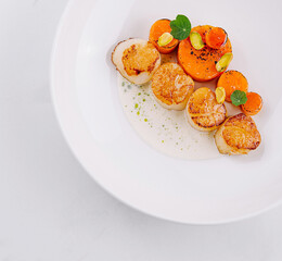 Seared scallops plate garnished with carrot and pistachio being served in a restaurant